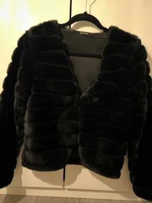 Svart pälsjacka från Gina Tricot XS - Säljer en fluffig svart pälsjacka från Gina Tricot i storlek XS. Jackan har en croppad modell, hakknäppning framtill och breda, mjuka paneler som ger en lyxig känsla. Perfekt för dig som vill ha en statementjacka till hösten eller vintern.