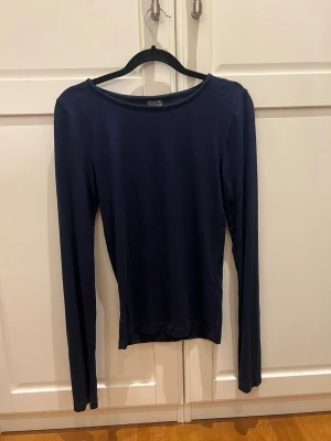 Mörkblå långärmad topp med slits - En enkel och stilren mörkblå långärmad topp i mjukt bomullsmaterial. Toppen har en rund halsringning och unika slitsdetaljer vid ärmsluten som ger en extra touch. Perfekt att matcha med jeans eller kjol för en clean look.