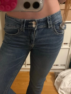 Blå low bootcut jeans - Snygga blå jeans med dubbla knappar i midjan och vita kontrastsömmar. Klassisk femficksmodell med en extra liten ficka framtill. Jeansen är i stl 164 och kommer helt enkelt inte till användning! 