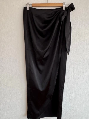 Svart omlottkjol med knytband - Stilren svart långkjol i omlottmodell med knytband i midjan och drapering. Använd fåtal gånger.