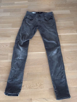 Replay Anbass grå jeans herr - Säljer ett par grå Replay Anbass jeans med slim passform. Klassisk femficksmodell med dragkedjegylf och snygga detaljer vid fickorna. Jeansen är tillverkade i mjuk bomullsblandning och har en modern, smal siluett som passar perfekt till streetwear. 29/32