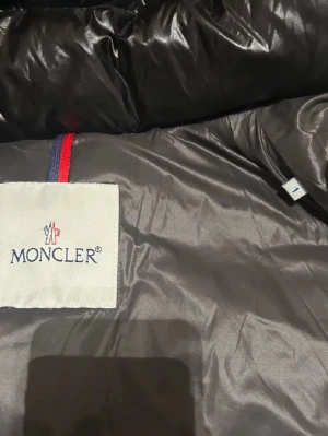 Svart dunjacka från Moncler - Snygg svart dunjacka från Moncler med klassisk quiltad design och dragkedja. Insidan har Monclers ikoniska etikett och serietidningsdetalj. Jackan har en glansig finish och är perfekt för kalla dagar. Nypris är 18,000kr men pris kan diskuteras 