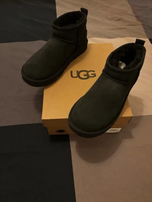 Svarta UGG Classic ultra mini - Svarta boots från UGG i mjuk mocka med rund tå och platt sula. Insidan är fodrad med päls för extra värme och komfort. Klassisk och enkel design som funkar till många olika outfits.