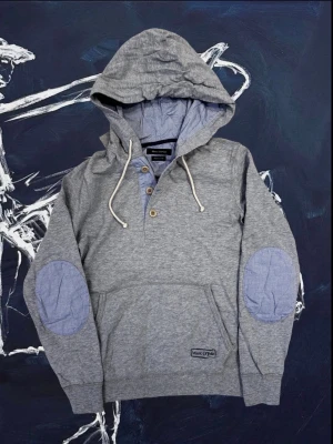 Grå hoodie från Marc O'Polo - Snygg grå hoodie från Marc O'Polo i mjuk ekologisk bomull. Modellen har ljusblå knappar, dragsko i huvan och ljusblå förstärkningar på armbågarna. Passar skitbra nu till höst med lager på lager. För mer info så är det bara att skriva!