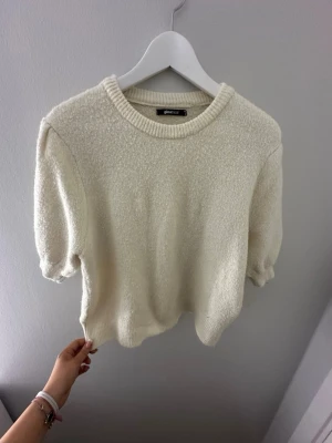 Krämvit stickad tröja Gina Tricot - Superfin krämvit stickad tröja från Gina Tricot med puffiga korta ärmar och rund hals. Tröjan har en mjuk och mysig struktur och ribbade detaljer vid hals och ärmslut. Perfekt till både jeans och kjol för en chill look.