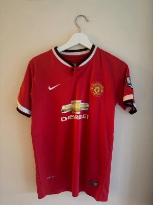 Manchester United Di Maria tröja - Säljer en röd Manchester United matchtröja från Nike med Di Maria och nummer 7 på ryggen. Tröjan har korta ärmar, vita och svarta detaljer vid krage och ärmslut samt Premier League-märke på ärmen. Tillverkad i lätt och ventilerande polyester.