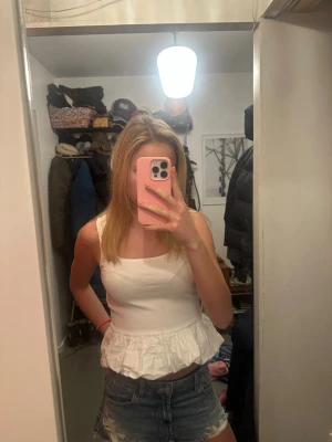 Vit volangtop med fyrkantig ringning - Säljer en söt vit topp med fyrkantig ringning och volang nertill. Toppen är ärmlös och har en croppad passform. Säljer pga att den inte kommer till användning. 