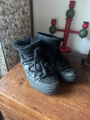Svarta Inuikii boots med snörning - Säljer ett par svarta boots från Inuikii med grov snörning och mjukt foder. Skorna har rund tå, platt sula och är tillverkade i skinn med insida i pälsimitation. Perfekt för kalla dagar! Använda under en vinter och säljer pga att de är för stora. 