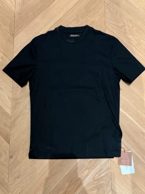 Svart t-shirt från Loro Piana - Snygg svart t-shirt från Loro Piana med diskret broderad logga i nacken och rund hals. Klassisk passform och mjukt material som känns lyxigt mot huden. Perfekt för dig som gillar stilrena och exklusiva plagg.