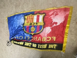 FC Barcelona flagga i rött och blått - Snygg FC Barcelona flagga med klubbens klassiska emblem i mitten. Flaggan har starka färger i rött, blått och gult, med texten 'THE BEST OF THE WORLD' och gul ram runtom. Perfekt för att visa ditt stöd för Barca!