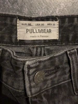 Svarta jeans från Pull&Bear, strl 36 W30 - Säljer ett par svarta jeans från Pull&Bear i storlek 36. Jeansen har klassisk femficksdesign, raka ben och knappstängning fram. Materialet är slitstark denim i bomull och färgen är mörkt tvättad svart med lite blekta detaljer för en cool look.