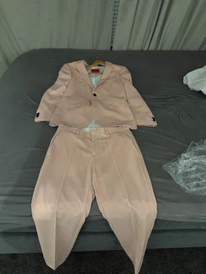 Ljusrosa kostym från Hugo - Säljer en stilren ljusrosa kostym från Hugo med klassisk kavaj och matchande byxor.n look. Priset är inte hugget i sten så kom med bud!!! (Kostymen är bara använd en gång) kostymen har pyttelite smuts längst ner på kavajen men går enkelt att tvätta bort.