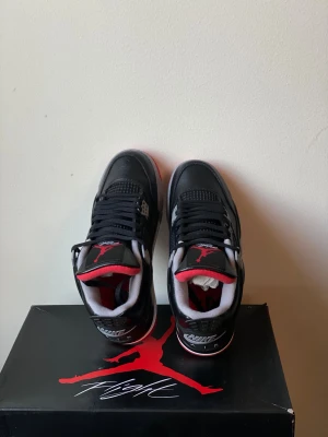 Nike Air Jordan 4 Black/Red - Nike Air Jordan 4 sneakers i svart och rött med grå och vita detaljer. Skorna har klassisk snörning, meshpaneler och synlig Air-sula. Ovandelen är i skinn och insidan har röd och grå vaddering. Ikonisk Jumpman-logga på plösen och Nike Air på hälen.