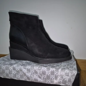 Svarta stövletter med kilklack - Säljer ett par svarta stövletter från RY med kilklack och dragkedja bak. Skorna har en snygg mix av mocka och skinn, vilket ger en cool kontrast. Rund tå och platt sula gör dem bekväma att bära. Perfekta för dig som gillar stilrena och moderna boots.