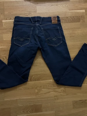 Replay Hyperflex Anbass jeans blå - Säljer ett par mörkblå Replay Hyperflex Anbass jeans med klassisk femficksdesign och snygga kontrastsömmar. Jeansen har slim passform, normal midja och stretchigt material som gör dem riktigt sköna. Märkespatch baktill och detaljerade bakfickor. 32/32 i storlek
