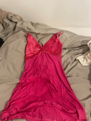 Rosa kortklänning med ribbad topp - Säljer en snygg rosa kortklänning med ribbad och v-ringad toppdel. Klänningen har smala axelband och ärmlös design, perfekt för varma dagar. Materialet känns mjukt och lätt, och den har en enkel, feminin siluett.