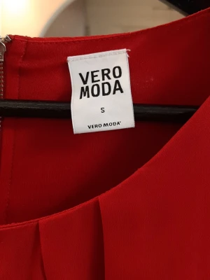Röd plisserad klänning Vero Moda S - Snygg röd klänning från Vero Moda i storlek S. Klänningen har plisserade detaljer framtill och en rund halsringning. Dragkedja i ryggen för enkel påklädning. Materialet känns lätt och faller fint.