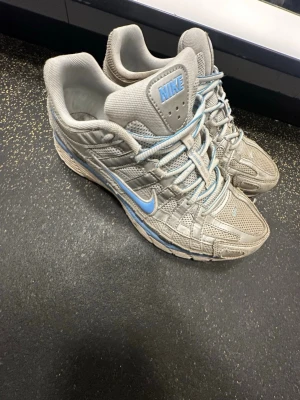 Nike P-6000 - Nike sneakers i grått mesh och syntet med blå swoosh och logga. Skorna har snörning och en sportig vibe, perfekt för dig som gillar streetwear. Snygga detaljer och bekväm passform med rund tå och platt sula.