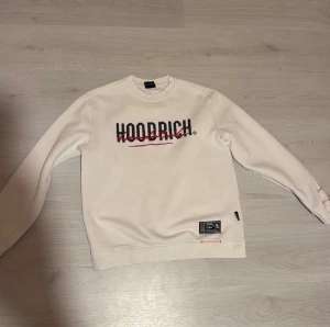 Vit sweatshirt från Hoodrich - Säljer en vit sweatshirt från Hoodrich med tryckt logga i svart och rött på bröstet. Använd fåtal gånger