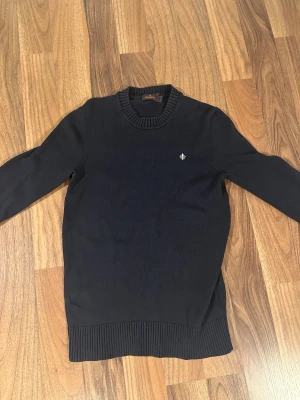 Morris stickad tröja storlek S - Mörkblå stickad tröja från Morris i modellen corby oneck med rund halsringning och diskret logga broderad på bröstet. Tröjan har ribbade muddar vid ärmslut och nederkant samt lång ärm. Perfekt för lager-på-lager under höst och vinter. Bra skick och är i storlek Small.