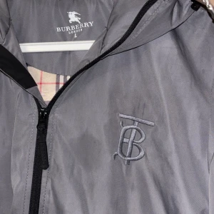 Grå vindjacka från Burberry - Uppgradera din vårstil med denna exklusiva Burberry-jacka – en perfekt kombination av lyx och funktion. Sitter som M. Tar byte 