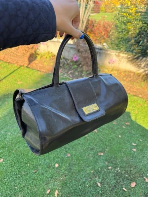 Brun handväska från Pettinati Italy - Snygg brun handväska från Pettinati Italy i äkta skinn med stilren, rektangulär form och två  handtag. Väskan har ett lock med magnetknäppning och en metallplakett med logga framtill. Perfekt storlek för dina essentials och ger en classy vibe.