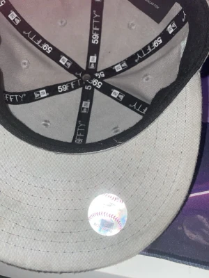 Grå LA 59FIFTY keps World Series - Säljer en grå 59FIFTY keps från New Era med LA-logga framtill och broderad 1988 World Series på sidan. Kepsen har en rak skärm och MLB-logga baktill. Materialet är bomull och kepsen har klassisk passform. Perfekt för dig som gillar baseball och streetwear. 