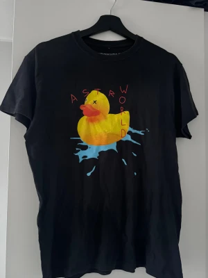 Astroworld svart t-shirt med tryck - Svart Astroworld t-shirt i bomull med färgglatt tryck av en gul badanka och texten 'ASTROWORLD' (Travis scott) på framsidan. Baksidan har tryck med 'LIVE', 'Wish you were here' och 'Europe 2019 World' i gult och turkost. Rund hals och korta ärmar, perfekt för dig som gillar streetwear.