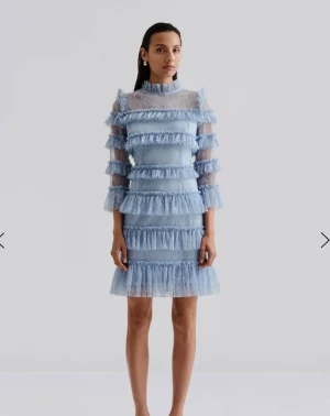 Nyskick Blå spetsklänning med volanger från Malina Stl xs - Superfin ljusblå kortklänning från Malina i spets med flera lager volanger och hög krage. Klänningen har trekvartsärm och är genombruten med romantisk känsla. Perfekt för dig som vill sticka ut med en unik och söt look.