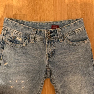 Ljusblå slitna jeans med bootcut - Ljusblå jeans med slitningar och distressed detaljer, dubbla knappar i midjan och bakfickor med broderier. Klassisk femficksmodell i bomull med bootcut-ben och cool vintagekänsla. Kan tyvärr inte visas på för att de är försmå.