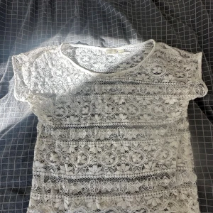 Vit spetsblus från Accessorize - Supersöt vit blus från Accessorize i storlek S. Helt i spets med blommigt mönster och korta ärmar. Perfekt för dig som gillar romantisk och feminin stil. Tunn och luftig, passar bra till både jeans och kjol.