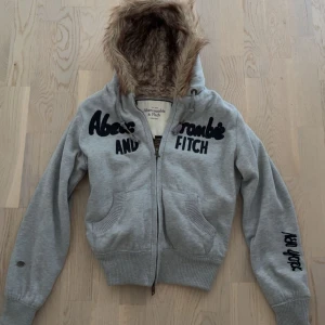 grå fuskpäls hoodie Abercrombie and fitch - Pälsfodrad zip-up jacka/hoodie från Abercrombie & Fitch i grått och storlek L, men sitter mer som en S! Väldigt fint skick! Broderad logga, dragkedja fram, sidofickor. Sällsynt vintage-plagg. Mindre lös tråd, visas på sista bilden.      #y2k #y2kfashion  #stylevintage #streetwear #abercrombieandfitch #abercrombie #abercrombiefitch  #aesthetic  #2000s #2000sclothing  #2000sfashion #niche  #lowwaist #vintage #rare #rarefind #2000style #vintage2000s #early2000s #furcoat #fur #furjacket #swag