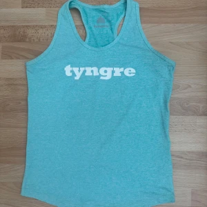 Turkos linnetopp från Tyngre XS - Säljer en turkos linnetopp från Tyngre i storlek XS. Toppen har brottarrygg och vit logga framtill. Tillverkad i mjuk och stretchig polyesterblandning, perfekt för träning. Snygg och sportig look med enkel design.