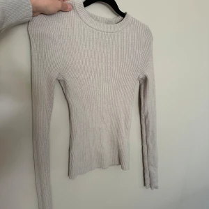 Beige ribbad stickad tröja H&M S - Säljer en beige ribbad stickad tröja från H&M i storlek S. Tröjan har lång ärm, rund halsringning och en slim passform. Perfekt för lager-på-lager och enkel att matcha med olika outfits.