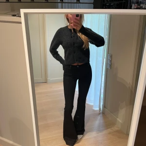 Mörkgrå stickad kofta med knappar - Säljer en mörkgrå stickad kofta med rund hals och stora knappar framtill. Koftan är croppad och har långa ärmar med ribbade muddar. 100% ull