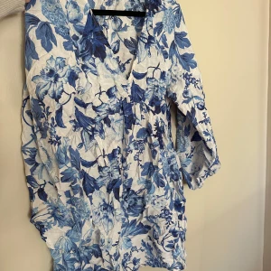 Blommig kortklänning från H&M XS - Supersöt kortklänning från H&M i storlek XS med blått och vitt blommigt mönster. Klänningen har v-ringning och långa ärmar, tillverkad i mjuk bomull som känns skön mot huden. Perfekt för dig som gillar romantiska vibes och fräscha färger.