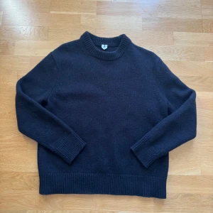 Svart stickad tröja i ull, Arket - En klassisk svart stickad tröja i ull med rund hals och breda ribbade muddar vid ärmslut och nederkant. Perfekt för kyliga dagar och enkel att matcha med jeans. Snygg och tidlös modell som passar till många olika stilar.