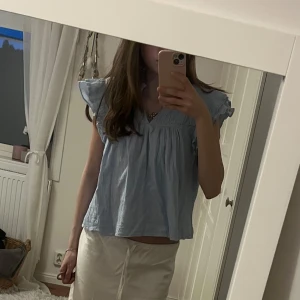 Ljusblå blus med volang från Gina Tricot - Supersöt ljusblå blus från Gina Tricot med v-ringning, volangdetaljer på ärmarna och spetsinslag. Blusen är ärmlös med en luftig och flowy passform. Tillverkad i mjuk bomull som känns skön mot huden. Köpt från barnavdelningen storlek 158/164 men skulle säga att den passar XS. Tveka inte att höra av dig om du har frågor😇