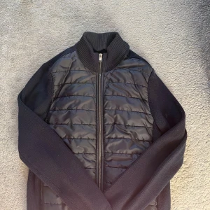 Mörkblå cardigan - Mörkblå cardigan med quiltad framsida och stickade ärmar. Perfekt för kyliga dagar och enkel att matcha med andra plagg.