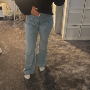 Ljusblå bootcut jeans med fickor - Säljer ett par ljusblå jeans med bootcut-modell och stora fyrkantiga fickor fram och bak. Jeansen har hög midja och är i klassisk denim med en snygg, avslappnad passform. Perfekta för dig som gillar retrovibbar och vill ha ett par trendiga jeans i garderoben.