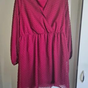 Vinröd kortklänning från SHEIN Curve - Superfin vinröd kortklänning från SHEIN Curve med omlott-v-ringning och långärmade transparenta ärmar. Klänningen har ett prickigt strukturmönster i tyget och är gjord i mjuk polyester. Perfekt för dig som gillar färg och vill sticka ut lite extra. Cool att dressa upp med boots och skinnjacka.  