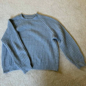 Blå stickad tröja från Lager 157 - Mysig blå stickad tröja från Lager 157 med grov struktur och ribbade muddar vid ärmslut och nederkant. Rund halsringning och långärmad modell, perfekt för kyliga dagar. Enkel och stilren design som funkar till allt.