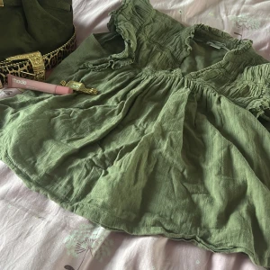 Grön blus med volangärm från Gina Tricot - Supersöt grön blus från Gina Tricot med v-ringning och volangdetaljer på ärmarna. Blusen är luftig och har rynkade partier upptill samt korta ärmar med volang. Perfekt för dig som gillar en avslappnad men ändå trendig look.