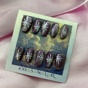 MidnightSnow (XS);Short Coffin;Curved - Handgjorda press-on naglar i storlek XS: 14 mm, 11 mm, 11,5 mm, 10 mm, 8 mm , har en glittrig cateye lila bas med vita handmålade stjärnmotiv. Formen är coffin och korta, kurvade och är lite mindre i storlek. Perfekt för dig som vill ha unika och snygga naglar utan att gå till salong.