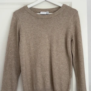 Beige stickad tröja från Vila - Mysig beige stickad tröja från Vila med rund halsringning och ribbade muddar. Perfekt för lager-på-lager och passar till allt. Enkel och stilren design som funkar året runt.