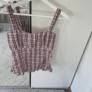 Rutig linnetopp från Dcate - Supersöt rutig linnetopp från Dcate i rött, beige och grönt. Toppen har breda axelband, smockad rygg och volangkant nertill. 