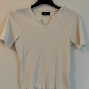 Vit ribbad topp från LMTD - Säljer en stilren vit ribbad topp från LMTD med korta ärmar och v-ringning med liten notch-detalj. Toppen är i stretchigt material och har en enkel, clean look som passar till många outfits.