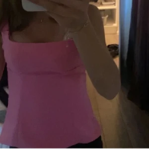 Rosa topp med rosett från Zara - Supersöt rosa linnetopp från Zara med breda axelband och en stor rosett i ryggen. Toppen har en rak, figurnära passform och är tillverkad i ett slätt polyestertyg. Perfekt för dig som vill sticka ut med en färgglad och feminin look. Köpte i somras testat på, säljer pågrund av att den är för liten💕