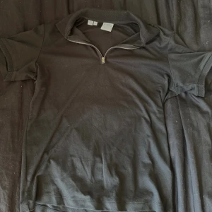 Svart pikétröja från Selected Homme - Svart pikétröja från Selected Homme med kort ärm och snygg krage. Tröjan har en modern half zip-dragkedja framtill och är gjord i mjuk bomull. Perfekt för dig som vill ha en stilren och bekväm look med lite edge.  Är villig att gå ner i pris. Skicka bud!