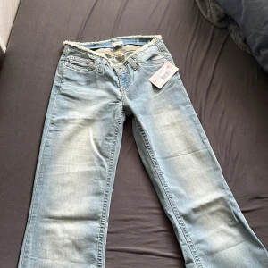 Ljusblå bootcut jeans från Nelly - Säljer ett par ljusblå bootcut jeans från Nelly med råa, fransiga kanter i midjan och vid bensluten. Jeansen har klassisk femficksdesign och är tillverkade i mjukt denimtyg. Perfekta för dig som gillar en avslappnad och trendig look. Köpte dom för 699 men säljer dom för 500